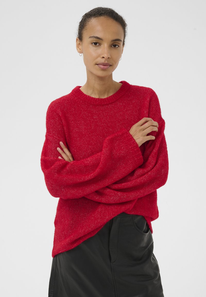 Punane ülisuuraga kootud kampsun tekstuurse viimistlusega, ümmarguse kaelusega ja laia varrukaga, kombineeritud musta nahast seelikuga.