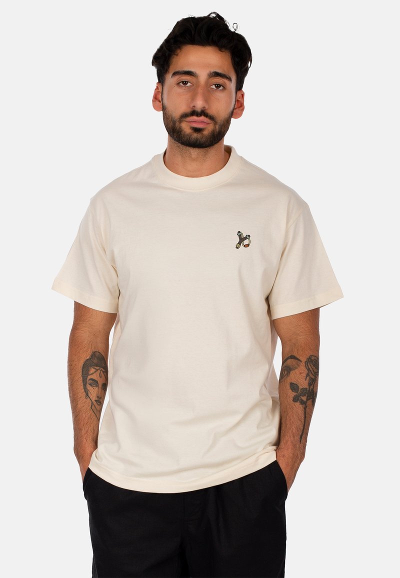 T-shirt in cotone crema a maniche corte, collo rotondo e una piccola grafica nella zona sinistra del petto. Vestibilità rilassata.