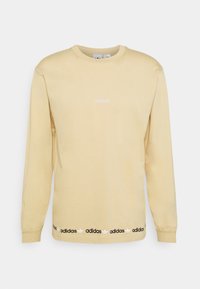 Ljusgul långärmad sweatshirt med rund halsringning. Har en central logotyp i vitt och en svart varumärkesdetalj vid fållen. Slät textur.