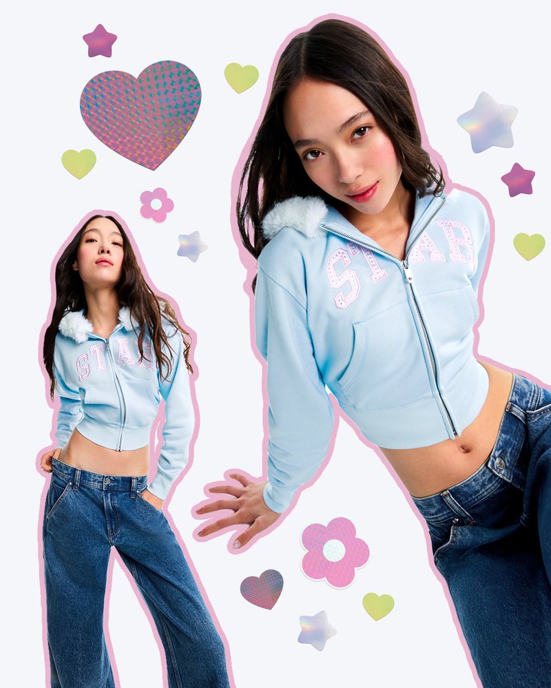 Sweatshirt azul curto com capuz felpudo, texto em lantejoulas "ESTRELA", combinado com jeans de perna larga. O fundo inclui formas geométricas coloridas.