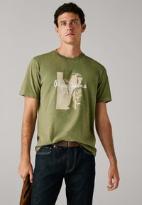 Olijfgroene katoenen T-shirt met ronde hals, korte mouwen en een grote licht beige grafische afbeelding met de tekst "Pepe Jeans London."