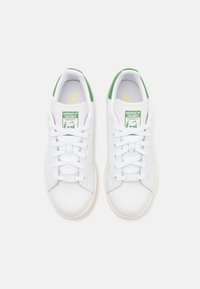 Ein Paar weiße Adidas Stan Smith Sneaker mit grünen Fersentabs und Logo auf der Zunge, von oben auf einem schlichten Hintergrund betrachtet.
