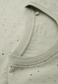 Lichtbeige t-shirt met een ronde hals, korte mouwen en een gespikkeld patroon in zwart en blauw. Zachte stoffen textuur.
