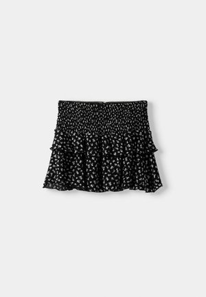 Falda negra con estampado floral y patrones blancos, con volantes en capas y una cintura fruncida, hecha de una tela ligera y texturizada.