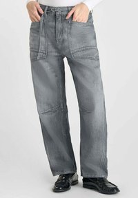 Pantalons en denim gris avec une coupe décontractée, dotés de plusieurs poches, d'une taille à passants de ceinture et d'une texture lisse. Des chaussures noires complètent la tenue.