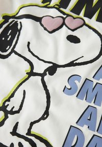 Hvitt stoff med en tegneseriehund med svarte konturer, iført rosa solbriller i form av hjerter, sammen med fet blå tekst.