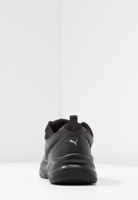 Chaussure de sport noire avec une tige synthétique, un détail texturé, un col rembourré et une semelle en caoutchouc. Présente un petit logo blanc sur le talon.