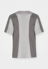 T-shirt gris et gris clair à manches courtes avec des panneaux latéraux contrastés et des détails de couture. Texture douce, design à col rond.