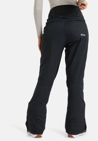 Zwarte sneeuwbroeken met een hoge tailleband, dubbele achterzakken en ritsen bij de enkels voor een verstelbare pasvorm. Roxy-logo op de achterkant.