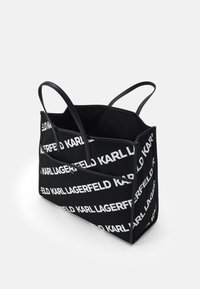 Svart canvas tote-väska med vitt textmönster "KARL LAGERFELD". Har dubbla svarta handtag och en strukturerad form med öppen topp.