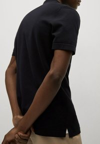 Musta lyhythihainen poolopaita, jossa siisti kaulus ja sivuhalkiot. Sileää kangasta ja vartalonmyötäinen malli. Yhdistetty beigen värisiin housuihin.