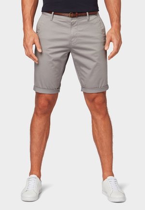 Pantaloni corti in cotone grigio chiaro con orli arrotolati, tasche frontali e dettagli per passanti della cintura, abbinati a sneakers bianche.