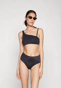 Conjunto de bikini preto com um top de um ombro só e calções de cintura alta, feito de um tecido suave com costuras mínimas e um design elegante.