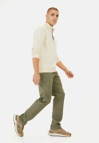 Crème trui met kraag en halve rits, gecombineerd met olijfgroene broek en bruine sneakers. Glad textuur, minimalistisch design.