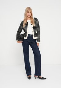 Μαύρο και άσπρο σακάκι με σχέδιο και στρογγυλά κουμπιά, συνδυασμένο με σκούρα τζιν παντελόνια με ευθεία γραμμή και μαύρες μυτερές γόβες.