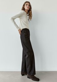 Zwarte wijde jeans met hoge taille, gecombineerd met een wit shirt met lange mouwen. De textuur is glad, terwijl de jeans achterzakken heeft.