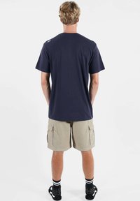 T-shirt en coton bleu marine à manches courtes, col rond, design uni, porté avec un short cargo beige et des chaussettes rayées noir et blanc.