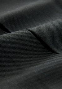 Črn material z drobno rebrasto teksturo, ki prikazuje mehke draperije in rahlo sijaj. Material deluje gosto in trpežno.