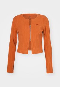 Chaqueta naranja de cremallera con canalé, de manga larga, diseño corto, cuello redondo y cremallera plateada con un tirador circular. Logo de Nike en burdeos oscuro.
