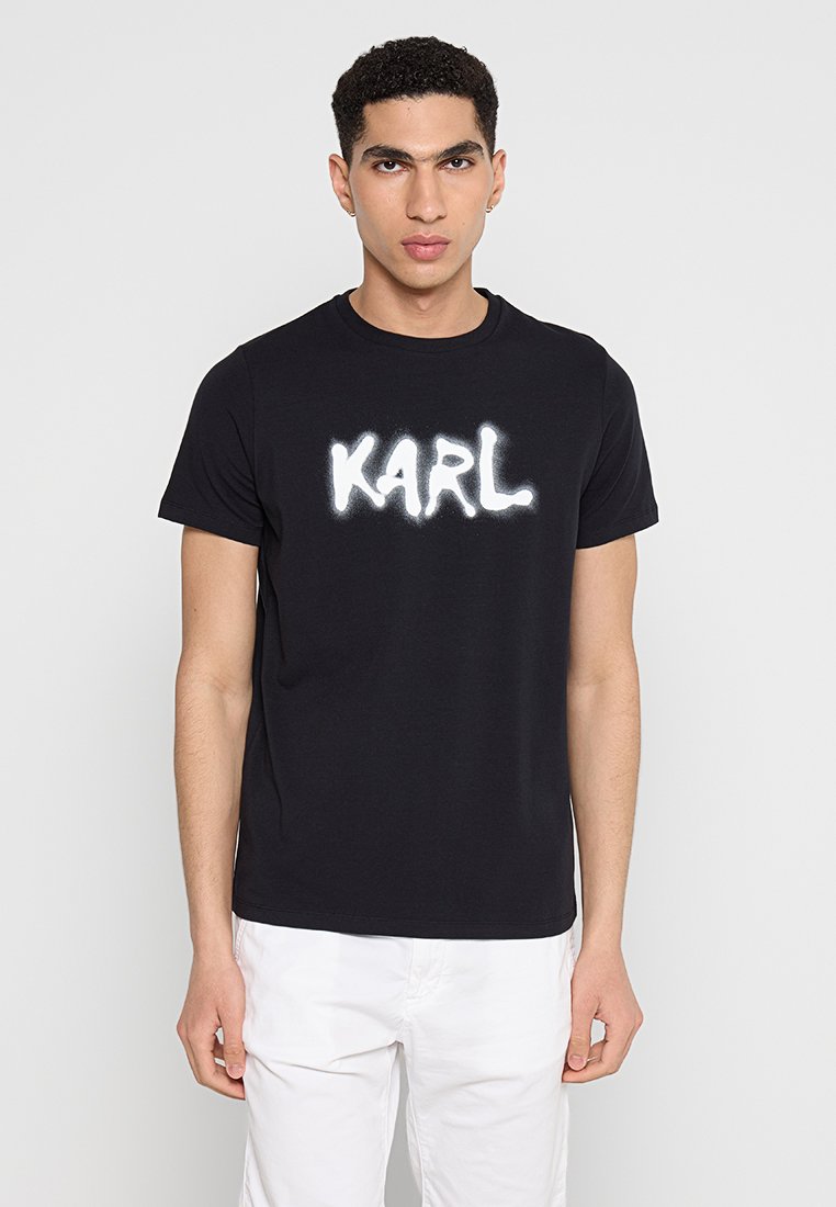 T-shirt en coton noir à manches courtes et col rond. Présente un logo "KARL" en peinture en spray blanche sur la poitrine.