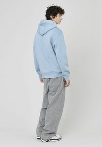 Un sweat à capuche bleu clair avec une coupe décontractée, une capuche à cordon et des poignets côtelés. Associé à un pantalon en denim gris ample et des baskets blanches.