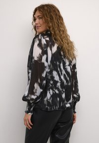 Zwart-wit geplisseerde blouse met vloeiende mouwen, voorzien van een abstract patroon en elastische manchetten, gecombineerd met zwarte gestructureerde broek.