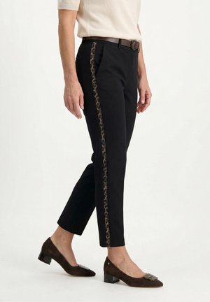 Person wearing black tapered pants with leopard print side stripes, brown belt, beige top, and brown low-heeled shoes with buckle detail.