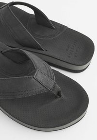 Sorte flip-flops med en formet fodseng, teksturerede gummistropper, perforeret overdel og let hævning ved hælen med en grå accentstribe.