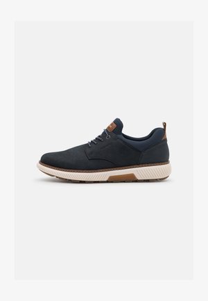 Chaussures en daim bleu marine avec un panneau noir texturé, des accents marron, une semelle intermédiaire blanche et des lacets gris, dotées d'un bout rond et d'une conception robuste.
