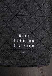Tissu gris foncé avec motif de grille géométrique noire et texte blanc "NIKE RUNNING DIVISION" centré sur la surface.