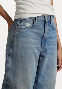 Ljusblå denimjeans med avslappnad passform, som har slitna detaljer, hög midja och metallbeslag vid fickan och gylfen.