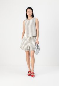 Striped linen top and shorts set in beige with black stripes, featuring a relaxed fit, drawstring waistband, and paired with red shoes and a silver bag.