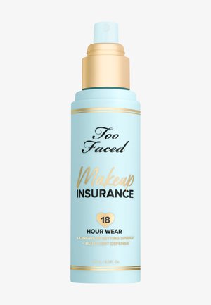 Un flacon pulvérisateur bleu clair avec des accents dorés, portant la mention "Too Faced Makeup Insurance" et des détails sur une tenue de 18 heures et une protection contre la lumière bleue.