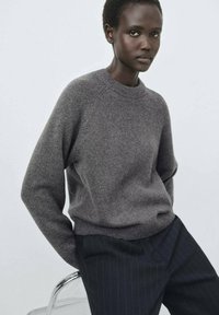 Grauer Wollpullover mit rundem Ausschnitt, gerippten Bündchen und Saum; kombiniert mit marineblauen, gestreiften Hosen. Glatte Textur und lockere Passform.