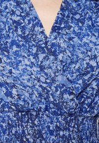 Blå mönstrad tyg har en blandning av ljusblå och mörkblå nyanser med en smocksmidda midja. Designen inkluderar en V-ringning och mjuk textur.