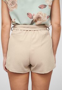 Pantaloni corti beige in tessuto testurizzato con dettaglio arricciato in vita, caratterizzati da una vestibilità rilassata e un orlo leggermente arcuato.