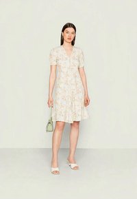 Vestido com estampa floral em cores pastéis claras, apresentando mangas curtas bufantes, decote em V e silhueta em A; combinado com uma bolsa verde-clara.