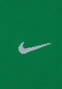 Tessuto a maglia verde con il logo Nike swoosh bianco. La texture è liscia con un motivo a maglia fitta e un colore vivace.