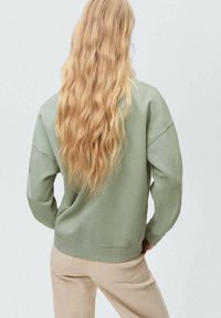 Lichtgroene sweatshirt met een ontspannen pasvorm en geribde manchetten, heeft een ronde halslijn en een gladde textuur, gecombineerd met lichtbeige broek.