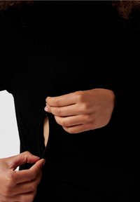 Top nero a maniche lunghe con apertura laterale con zip. Il tessuto sembra morbido e liscio, con un design aderente e uno stile minimalista.