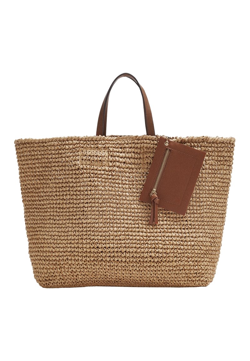 Sac de plage en paille tissée avec des poignées en cuir brun et une pochette zippée en cuir brun attachée sur fond blanc.