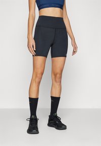 Shorts de sport noirs avec une taille haute, texture lisse et coutures contrastées. Assortis à des chaussettes noires et des chaussures de sport.