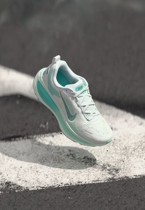 Lightweight running shoe in white with mint accents, mesh upper, textured surface, and prominent branding on the side. Floating above a pavement line.