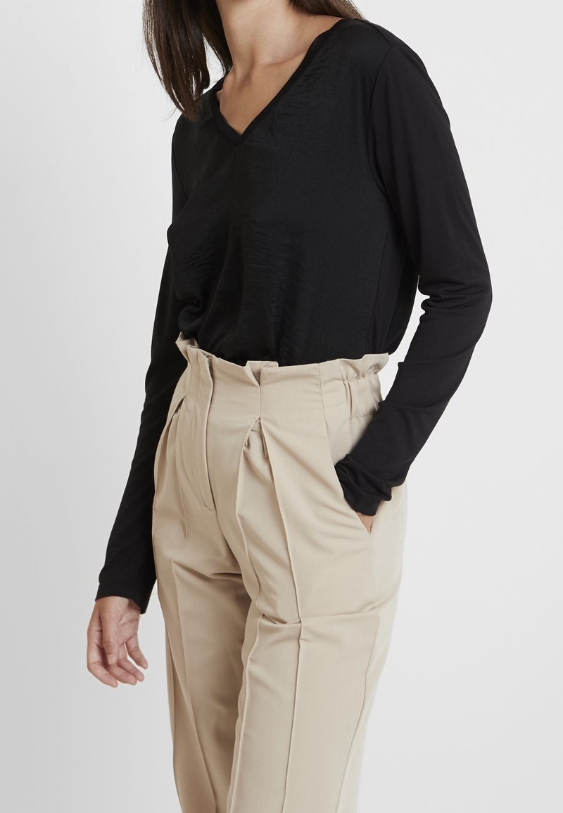 Černý dlouhý rukáv s výstřihem do V, doplněný o béžové kalhoty s vysokým pasem a sklady, které mají hladkou texturu a strukturovaný design.