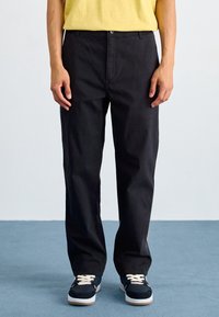 Svarta bomullsbyxor med rak passform, med framfickor och knappstängning. Matchas med marinblå sneakers och en gul skjorta.