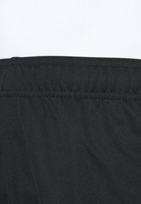 Zwarte stof met een gladde textuur, met een gatherband rondom de taille. Het ontwerp is eenvoudig zonder extra patronen of accenten.