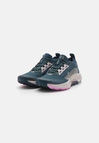 Zapatillas de trail running con una parte superior sintética en teal oscuro, paneles de malla gris, acentos rosas, suelas texturizadas y múltiples lazos de cordones.