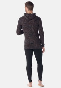 Hoodie mit langen Ärmeln und einem Labyrinthmuster in dunklen Farben, kombiniert mit schwarzen, engen Leggings; der Stoff wirkt glatt und leicht.