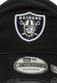Schwarze Baseballmütze mit verstellbarem Riemen, die auf der Vorderseite ein weißes und silbernes gesticktes Raiders-Logo sowie ein rundes New Era-Tag enthält.