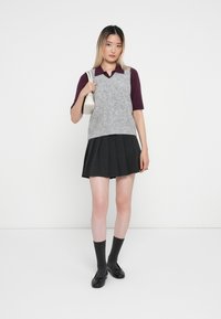 Sivý pletený sveter cez vínovú košeľu s golierom, doplnený skladanou čiernou sukňou. Čierne topánky a tmavosivé ponožky dopĺňajú outfit.